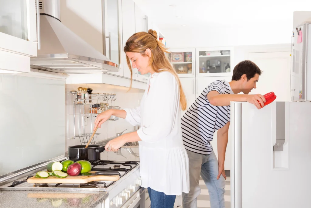 -smiling-woman-cooking-vegetables-while-her-husband-opening-refrigerator-door